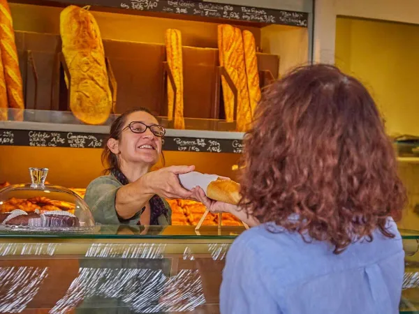 A lady gets baguettes from the bakery at Roan camping Les Dunes.