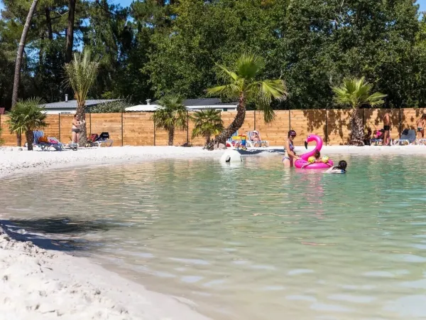 People sunbathing by the lagoon pool at Roan camping La Clairière.