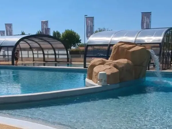 Covered swimming pool and outdoor pool with waterfall at Roan campsite Le Domaine du Clarys.