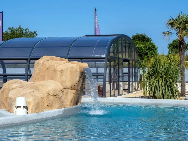 Covered swimming pool and outdoor pool with waterfall at Roan campsite Le Domaine du Clarys.