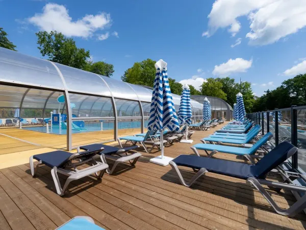 Sunbeds and parasols by the pool at Roan camping Le Lac des Vieilles Forges.