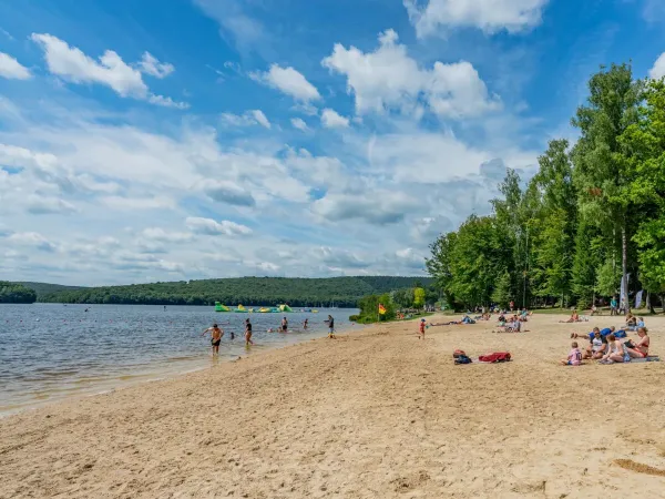 Families sunbathe on the lake beach at Roan campsite Le Lac des Vieilles Forges.
